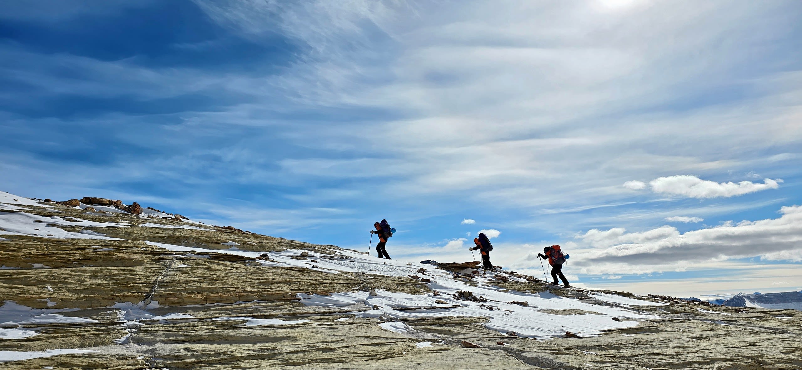 James Muirhead, Sandra Rodrigues and Zoe Armstrong silhouetted against the sky at Upper Wright Valley, climbing along a ridge to explore an outcrop.