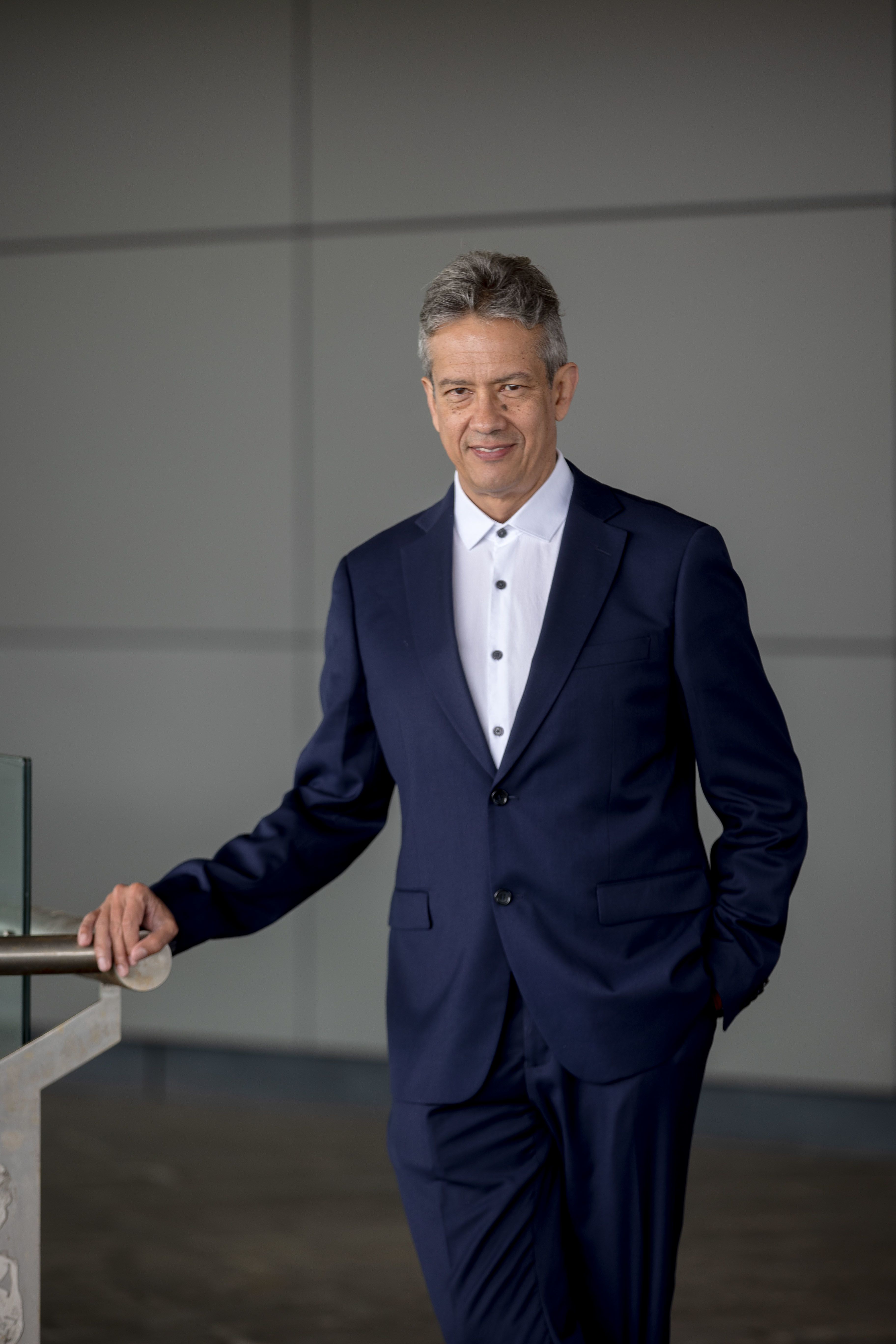 Professor Emilson Silva leaning his hand on a rail in front of a grey wall with rectangular sections